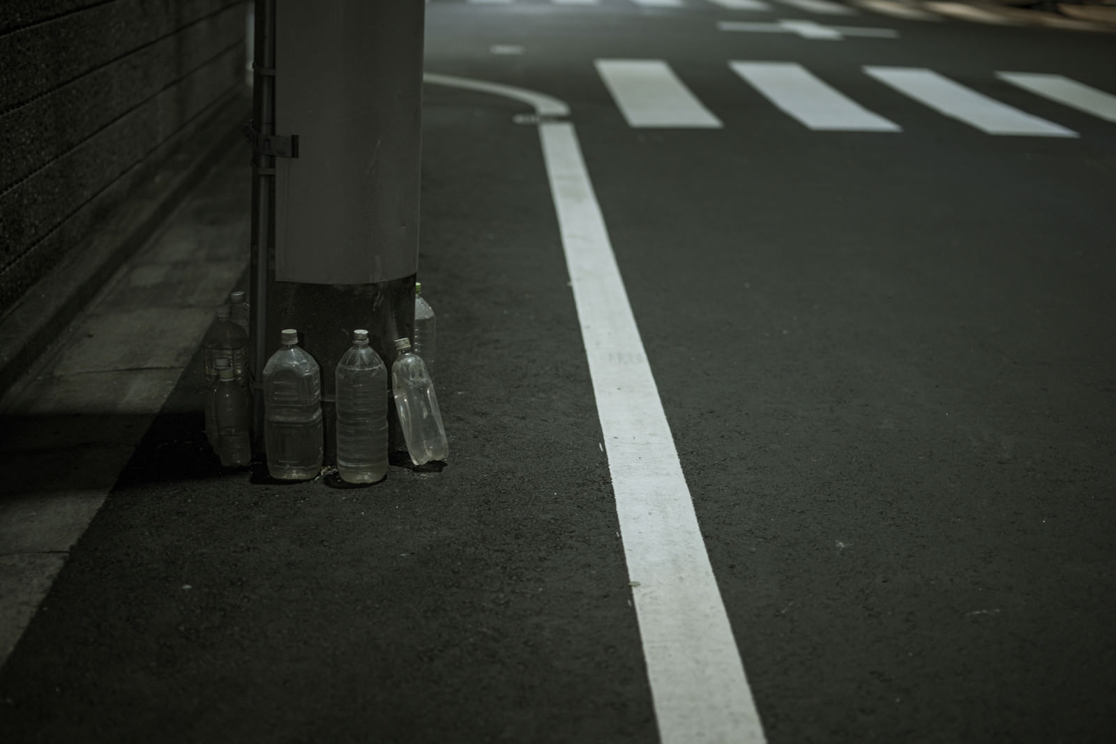 電柱の根元に置かれた透明なペットボトルと白線が引かれた歩道