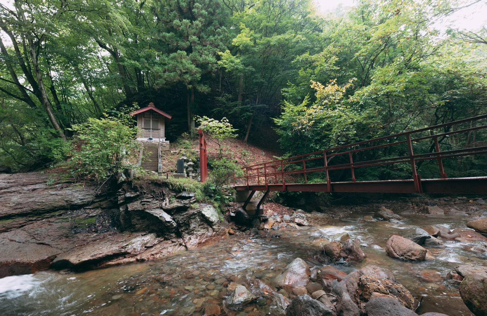 緑の森林に囲まれた渓谷に架かる木製の橋とその先にある神社