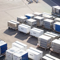 空港の滑走路に整然と並ぶ航空貨物コンテナの写真