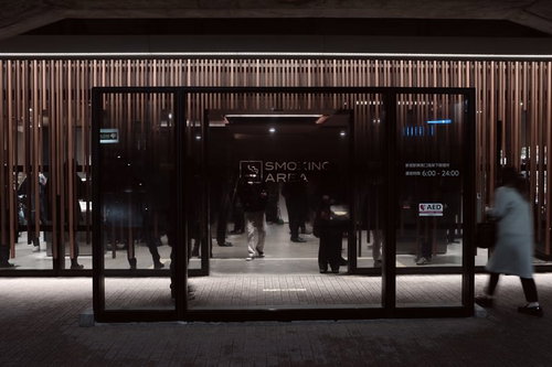 屋外の喫煙所でシルエットになる複数の人びと