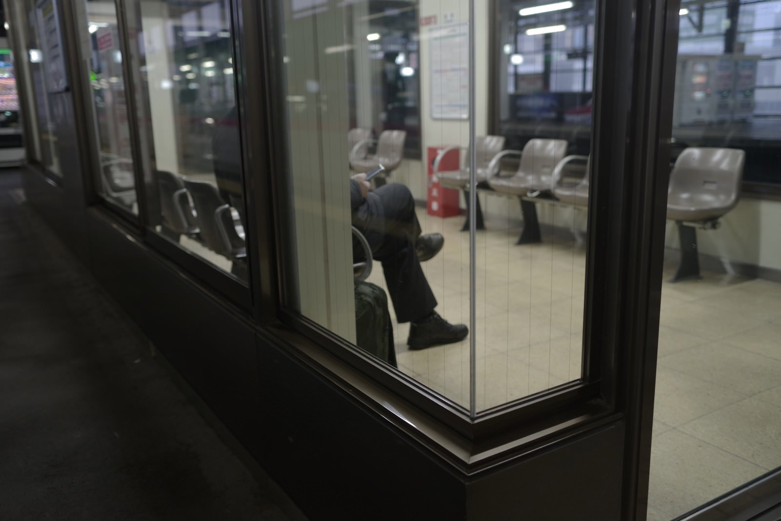 ガラス張りの電車待合室内でベンチに座る利用者たち