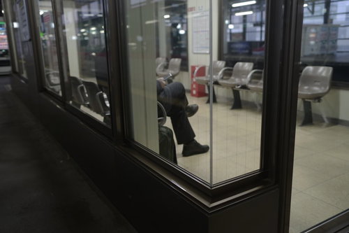 駅構内のホームにある待合室でベンチに座って電車を待つ乗客たち