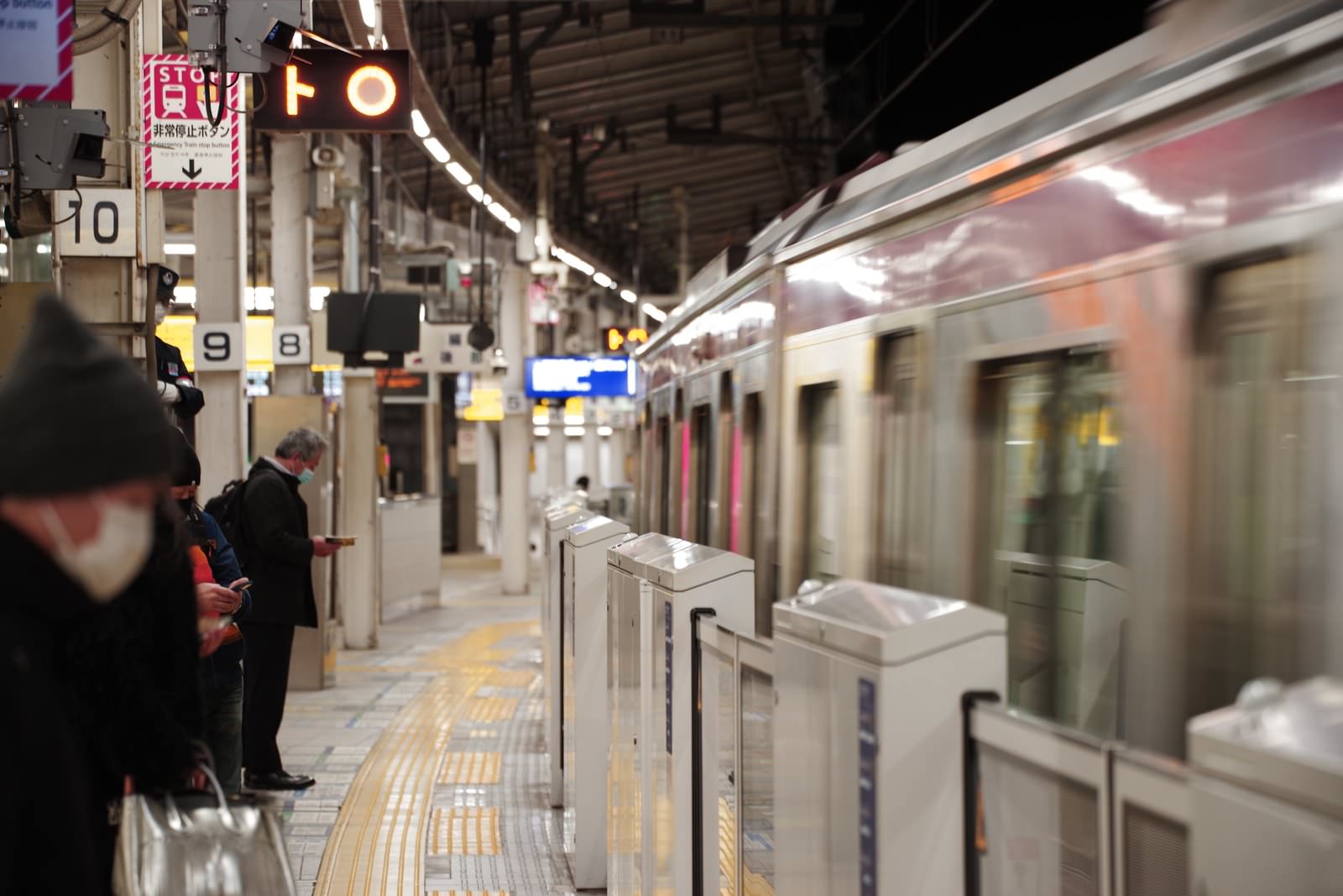 電車のホームで通過する電車を背景に待つ会社員たち