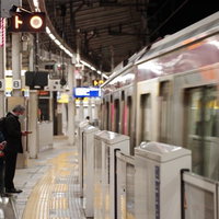 駅のホームで通過する電車を待つ会社員たちの写真