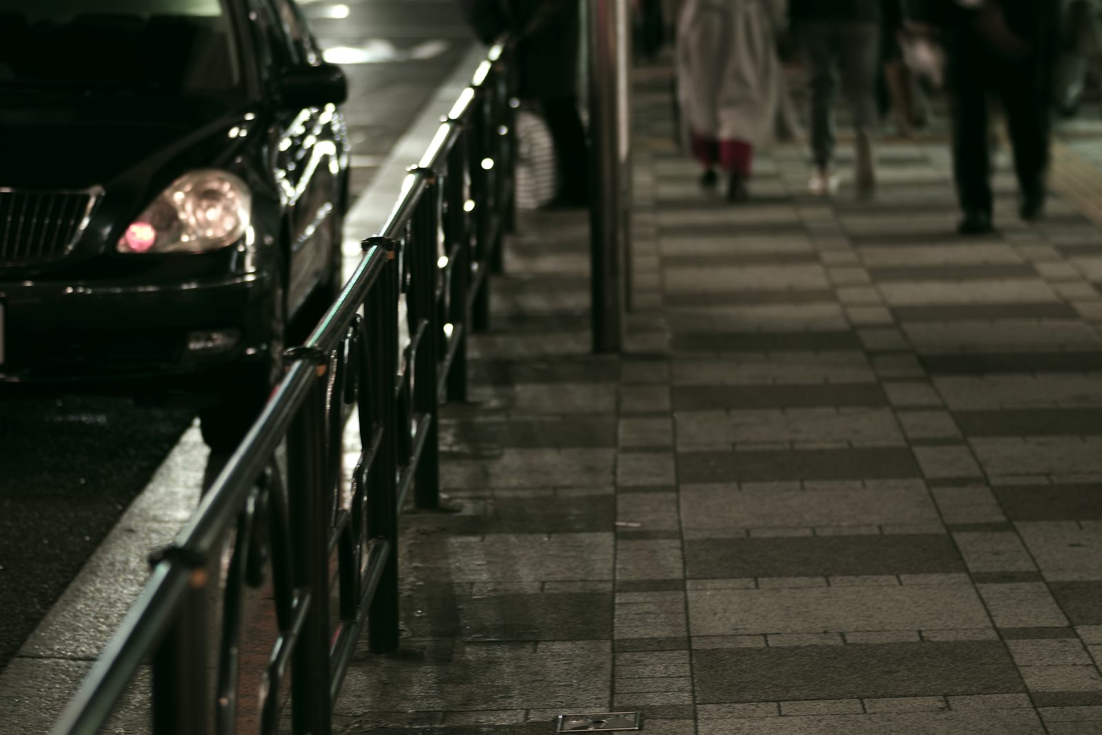 雨夜の歩道とガードレール越しの車