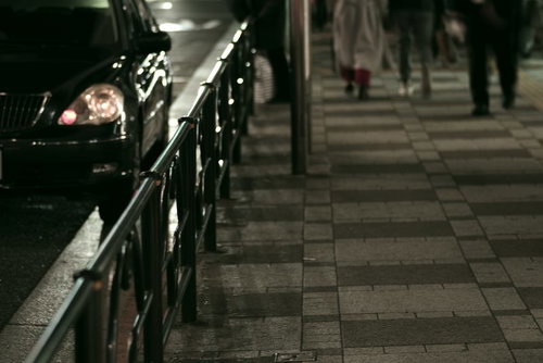 夜間の歩道で車のヘッドライトが反射するガードレール