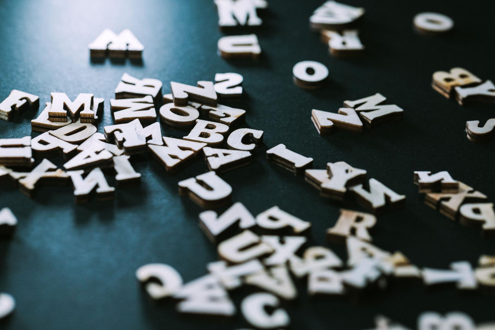 黒い背景に散らばった白い木製のアルファベットと数字