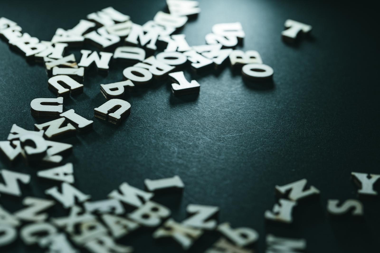 白い木製アルファベットが緑灰色の背景に散らばった写真