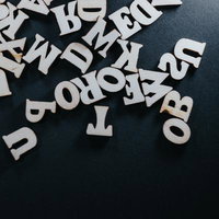 黒い背景に散らばる木製アルファベットパーツの写真