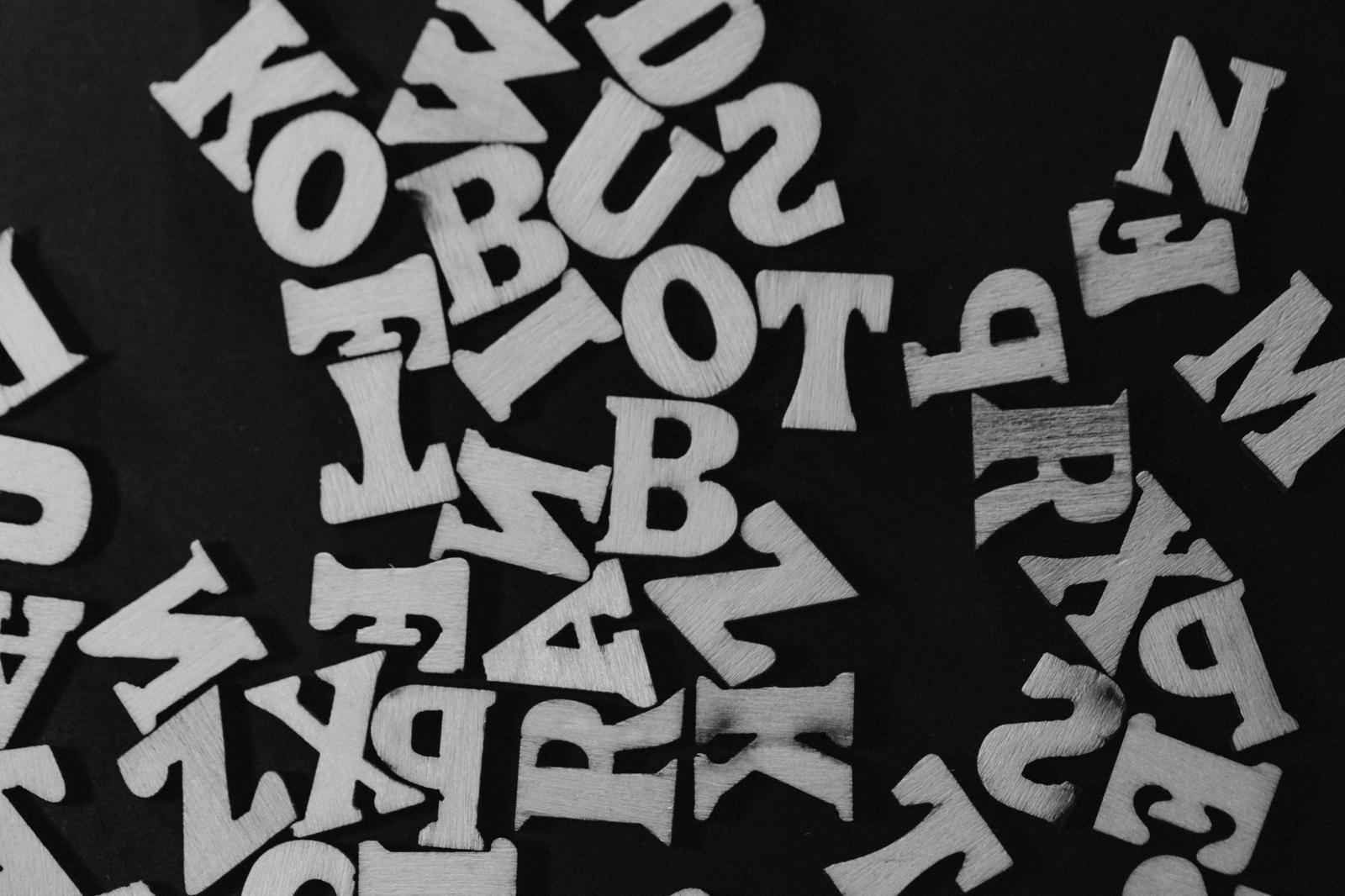 黒い背景の上にランダムに散らばった白い木製のアルファベットと数字
