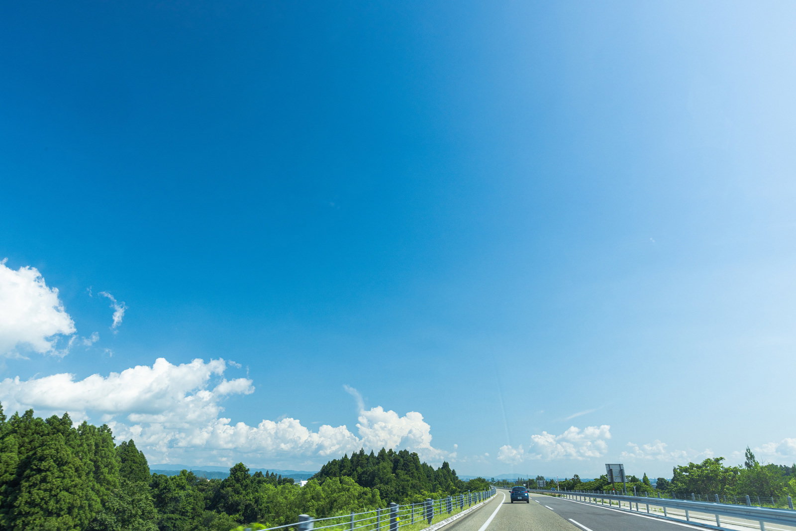 青空と白い雲が広がる高速道路をドライバー視点で撮影した写真