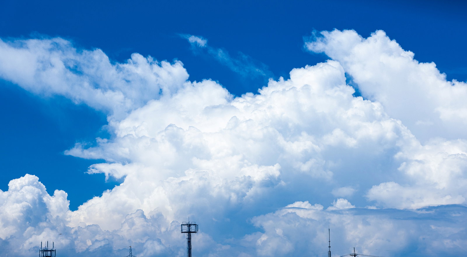 青空に大きく立ち昇る白い積乱雲と電柱のある夏日の風景