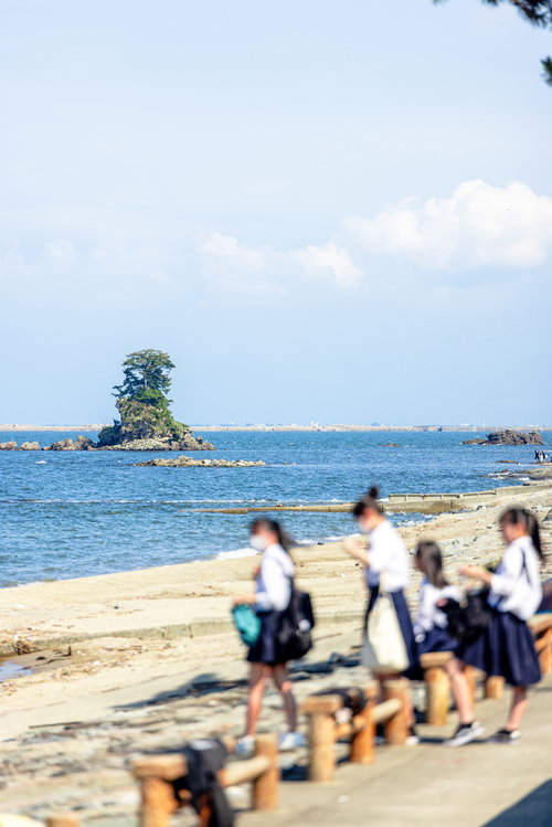 雨晴海岸の女岩を背景にした制服姿の女子学生たち