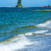 雨晴海岸の波打ち際に立つ女岩と押し寄せる波の写真