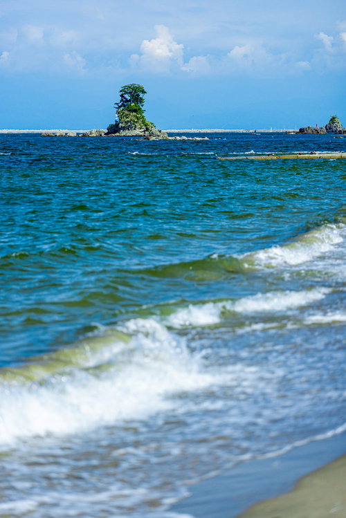 雨晴海岸の波打ち際に立つ女岩と押し寄せる波