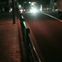 夜間の濡れた歩道に設置されたガードレールと走行車のヘッドライトの写真