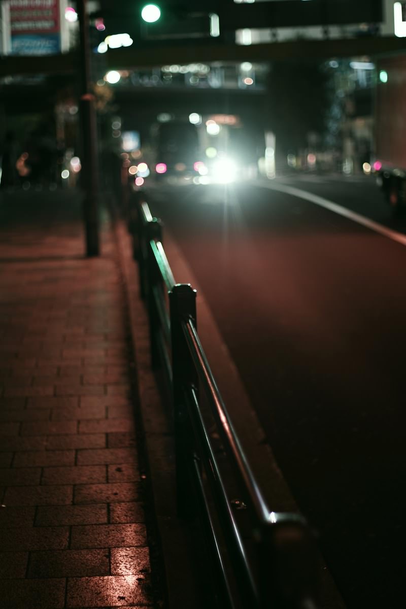 夜の濡れた歩道に設置されたガードレールと奥から照らす車のヘッドライト