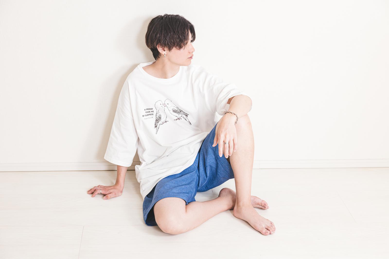 白いTシャツと紺のハーフパンツを着た男性が壁に寄りかかり座っている［モデル：SHUN］