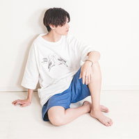 白いTシャツと紺のハーフパンツで壁に寄りかかる若い男性の写真