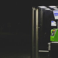 夜間の暗闇の中に浮かぶ緑の電話ボックスと街灯の写真