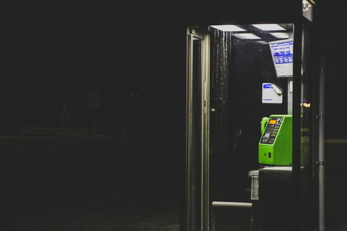 夜間の暗闇の中に浮かぶ緑の電話ボックスと街灯
