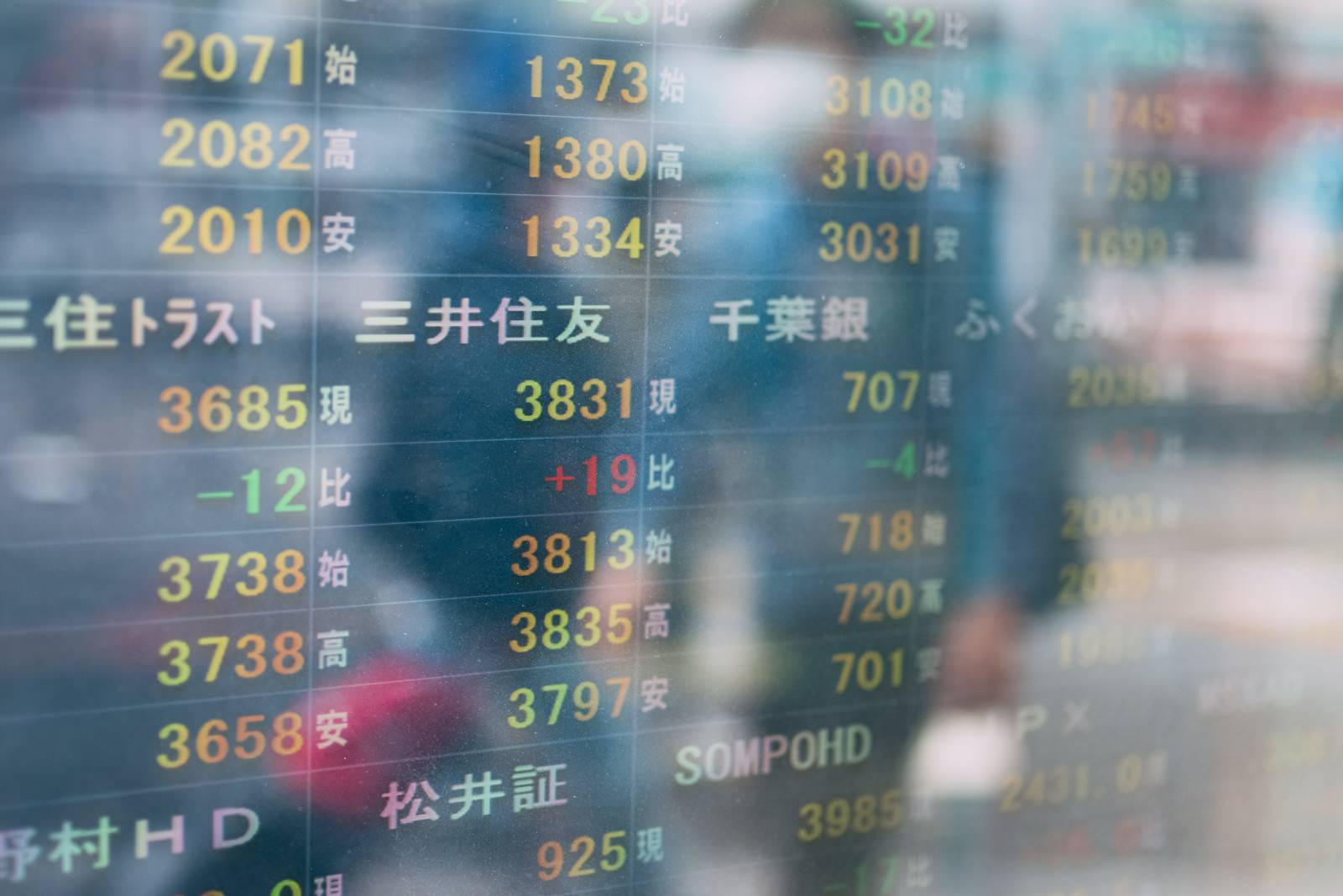 株価の数字が表示された電光掲示板に通行人の影が映り込んでいる様子