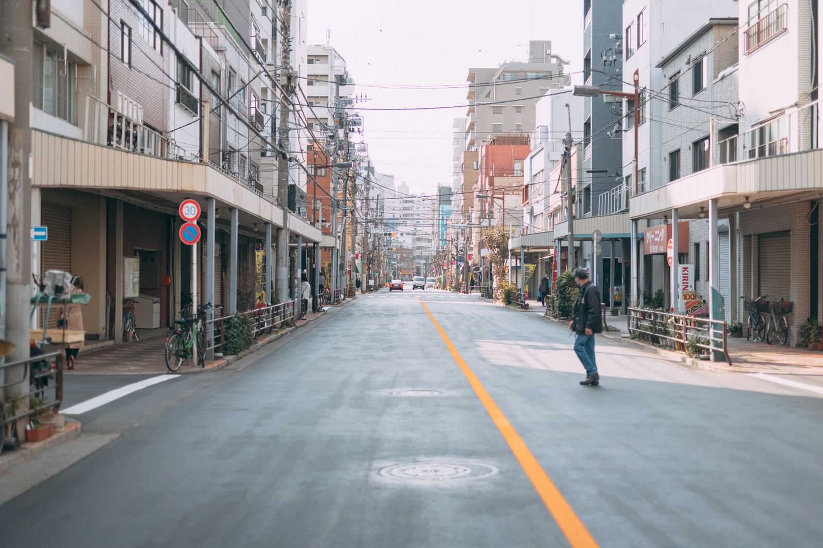 商店街の車道の中央を歩く通行人と両側に建ち並ぶ店舗