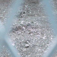 フェンス越しに見る灰色の砂利が敷かれた地面の写真