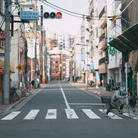 住宅街の道路で赤信号の横断歩道を自転車を押して横切る人の写真