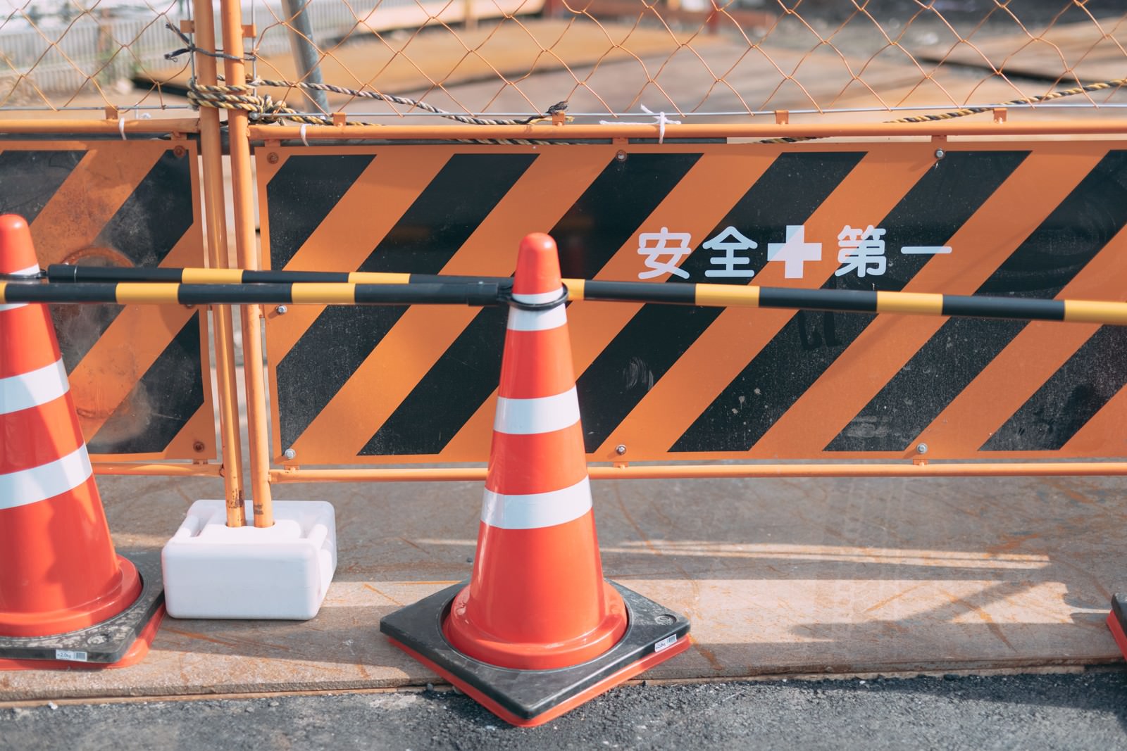 工事現場に置かれたオレンジ色の三角コーンとストライプ模様のフェンス