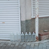 街角の白いシャッター前に並べられた猫除けのペットボトルの写真