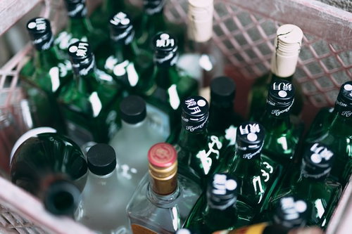 焼酎の空き瓶が積み重なる山、緑色ボトルが層状に保管された光景