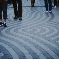 幾何学模様の広場に立ち並ぶ人びとのあしもとの写真