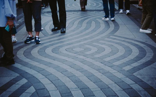 幾何学模様の広場に立ち並ぶ人びとのあしもと