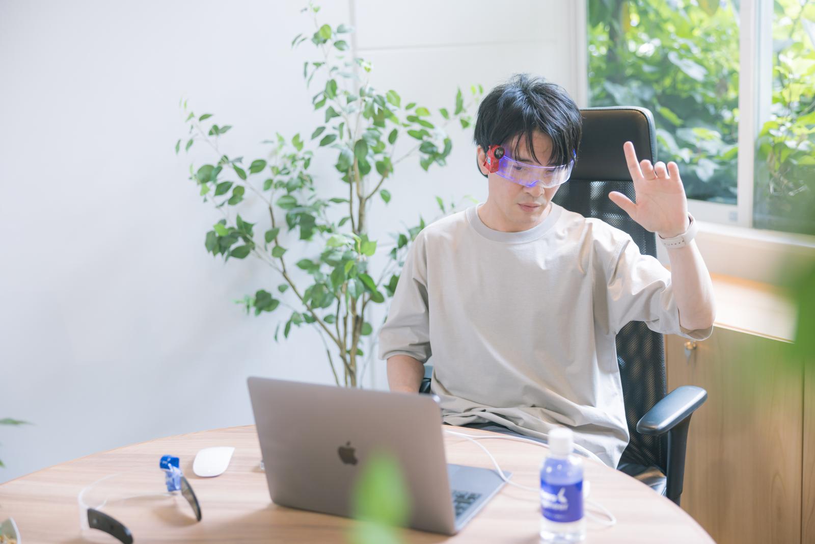 ARグラスをかけた男性がオフィスでジェスチャーにより画面操作している［モデル：金子周平］