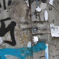 落書きとシールが剥がされたコンクリート壁と青いペイントの写真