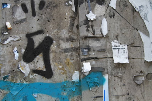 落書きとシールが剥がされたコンクリート壁と青いペイント