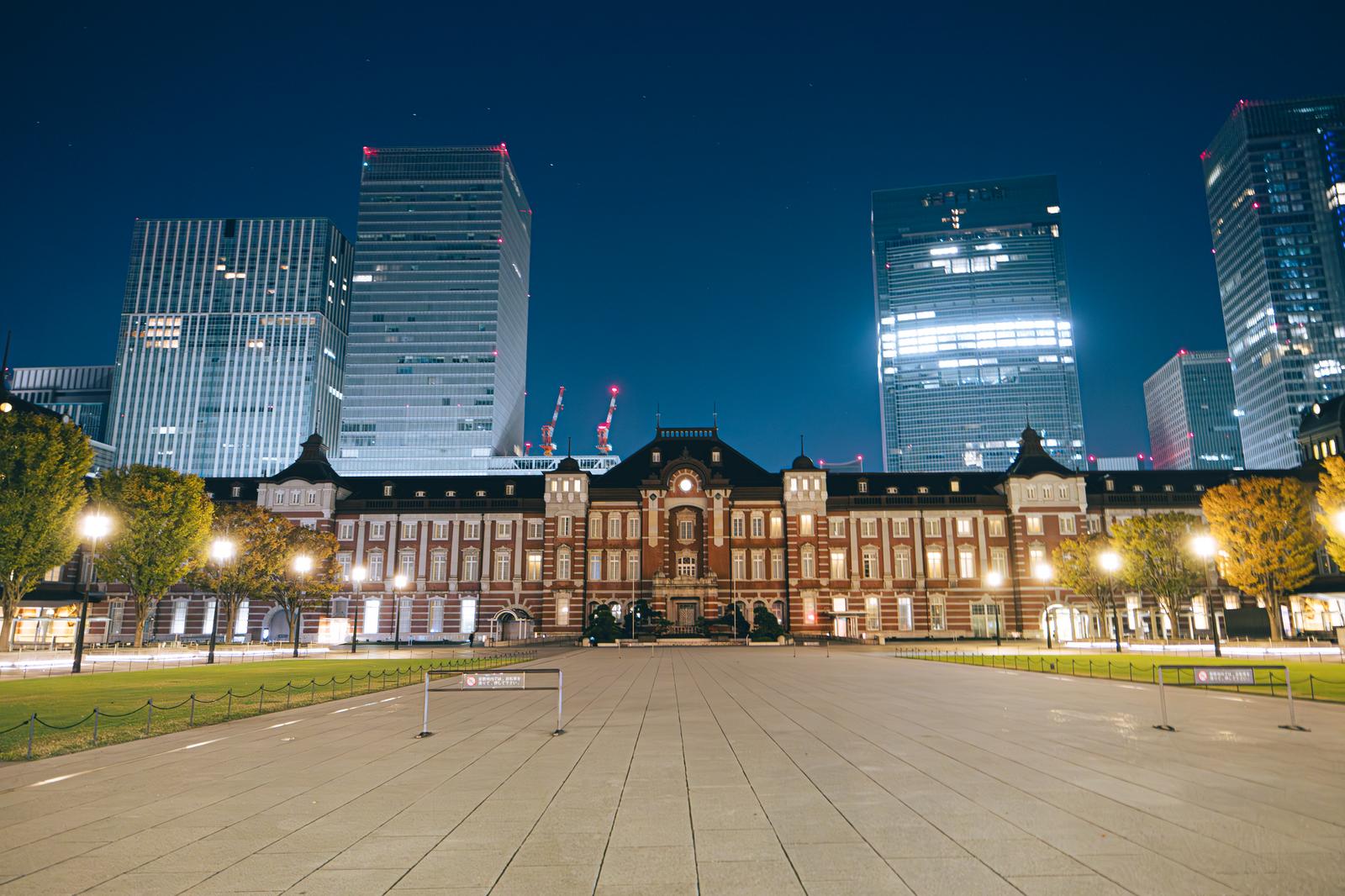 夜間にライトアップされた東京駅丸の内口の正面、高層ビルが背景