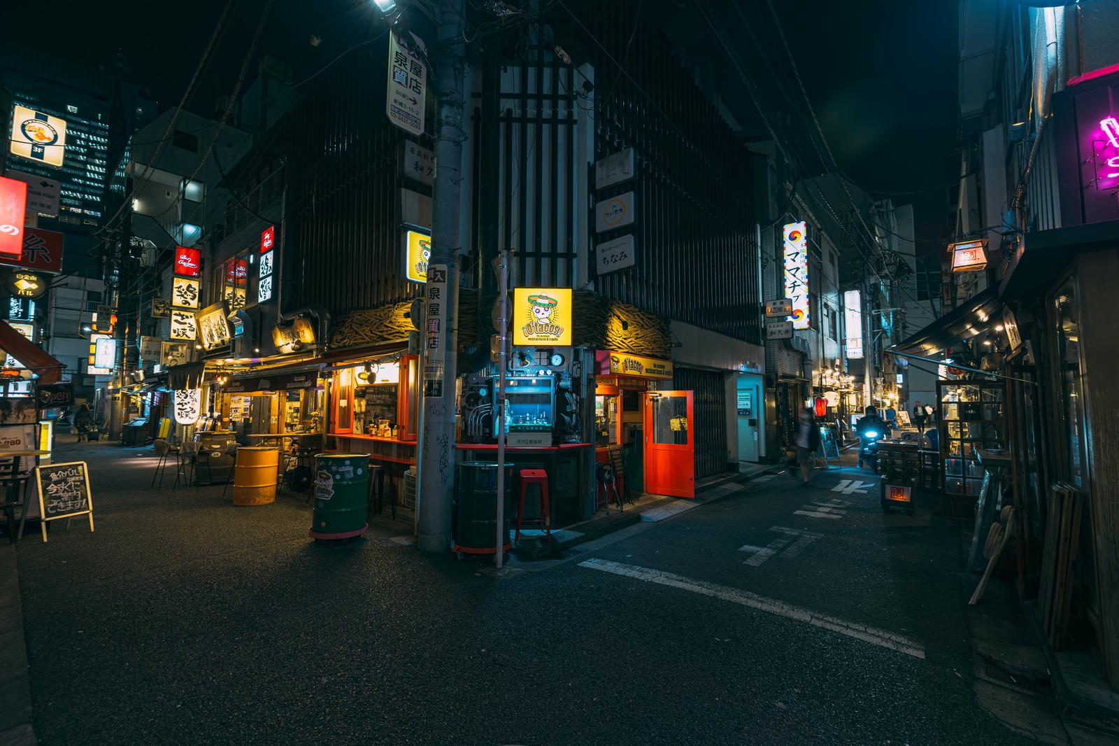 夜間の新橋の路地裏で、ネオン看板が点灯した飲み屋街の光景