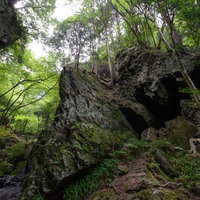 登山道に立ちはだかる岩の門と緑豊かな森林風景の写真