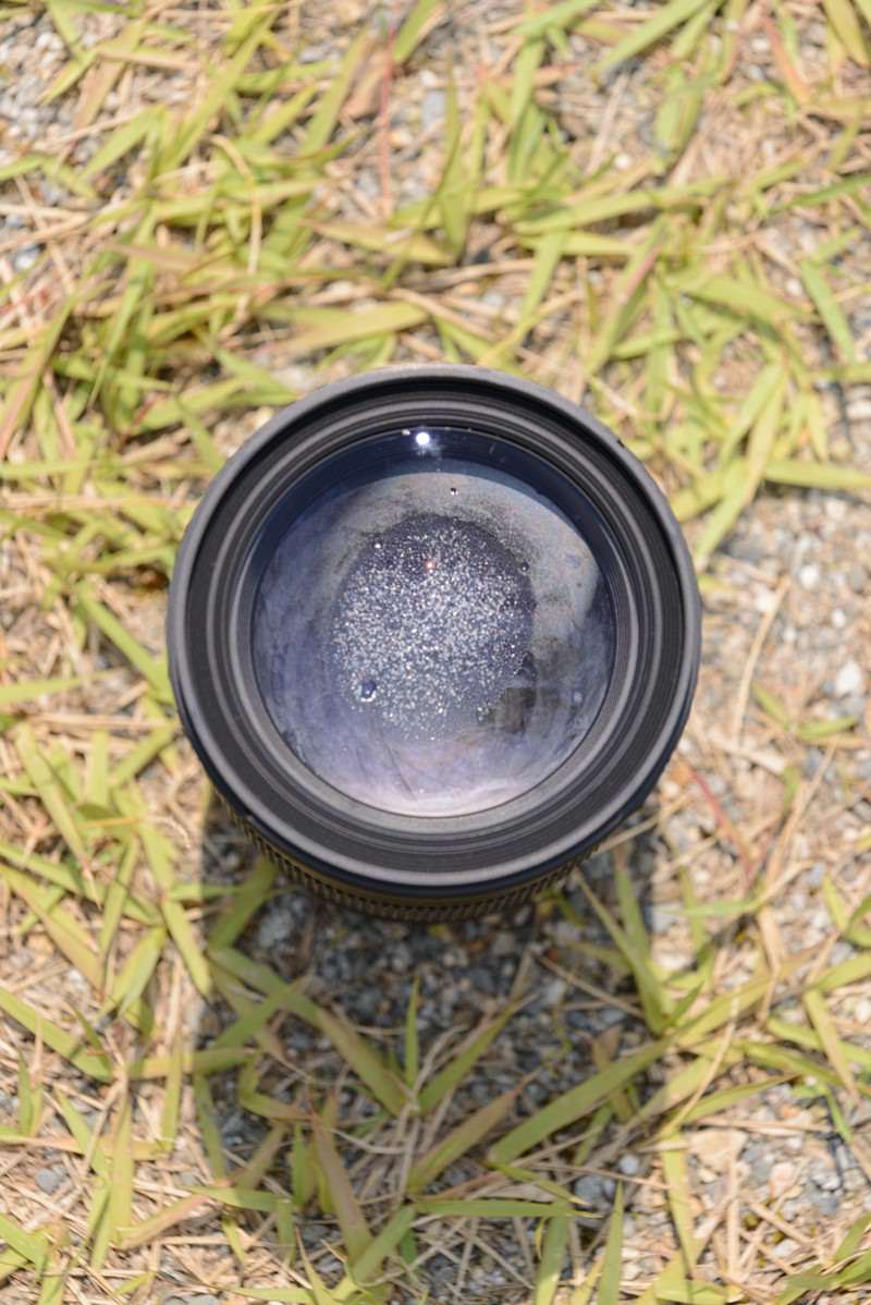 水没して内部に水滴が付着したズームレンズが草の上に置かれている