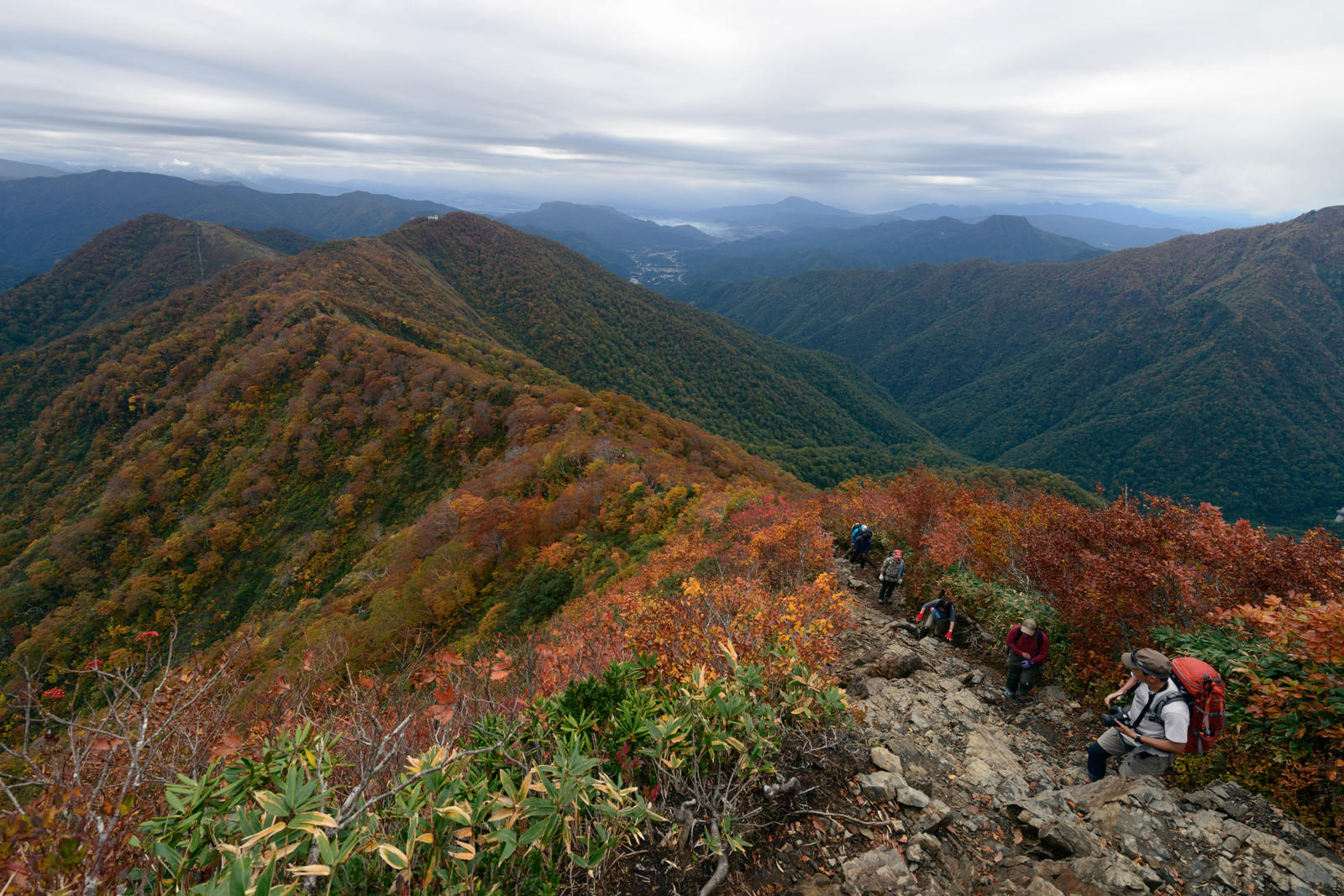 紅葉した谷川岳の稜線を歩く登山者と遠くに広がる山々の景色