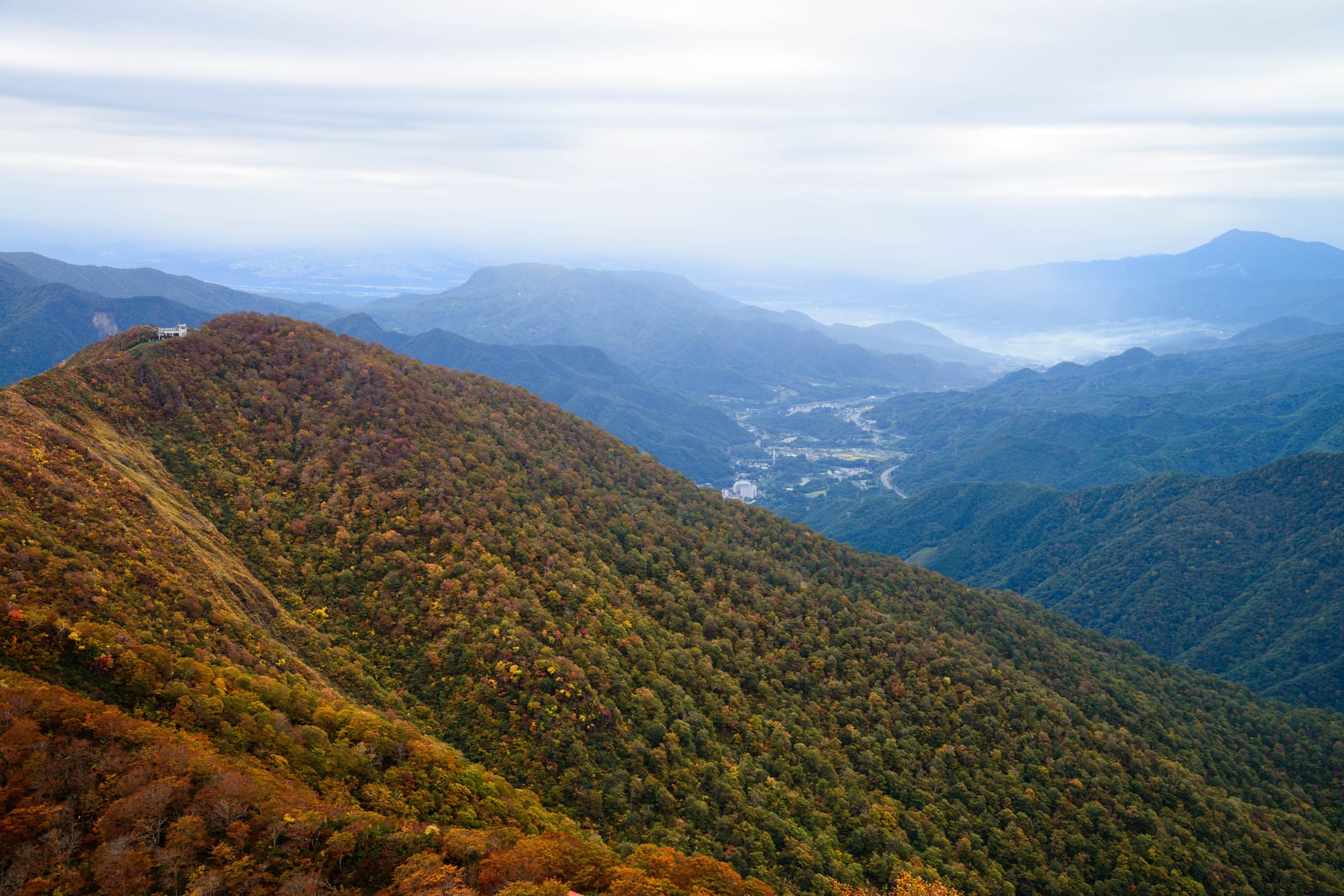 秋の谷川岳の山肌に広がる紅葉と黄葉、眼下に見える街並み