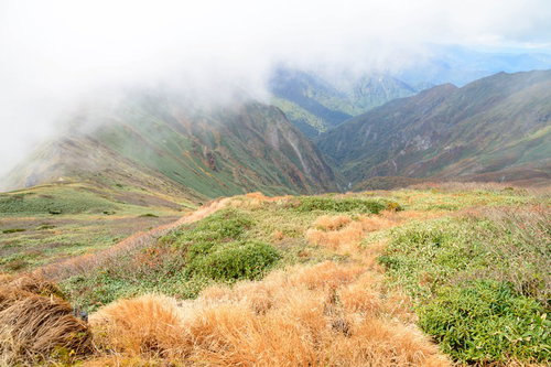 沸き立つガスに包まれた秋の谷川岳、枯れ草の山肌