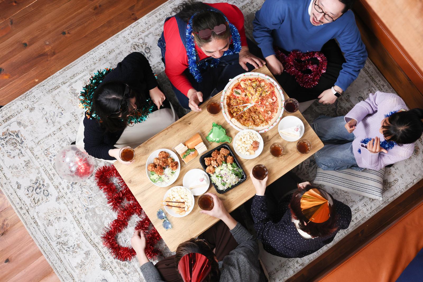 テーブルを囲んでピザを食べながら乾杯する家族［モデル：よたか ゆうせい あんじゅ 河村友歌］