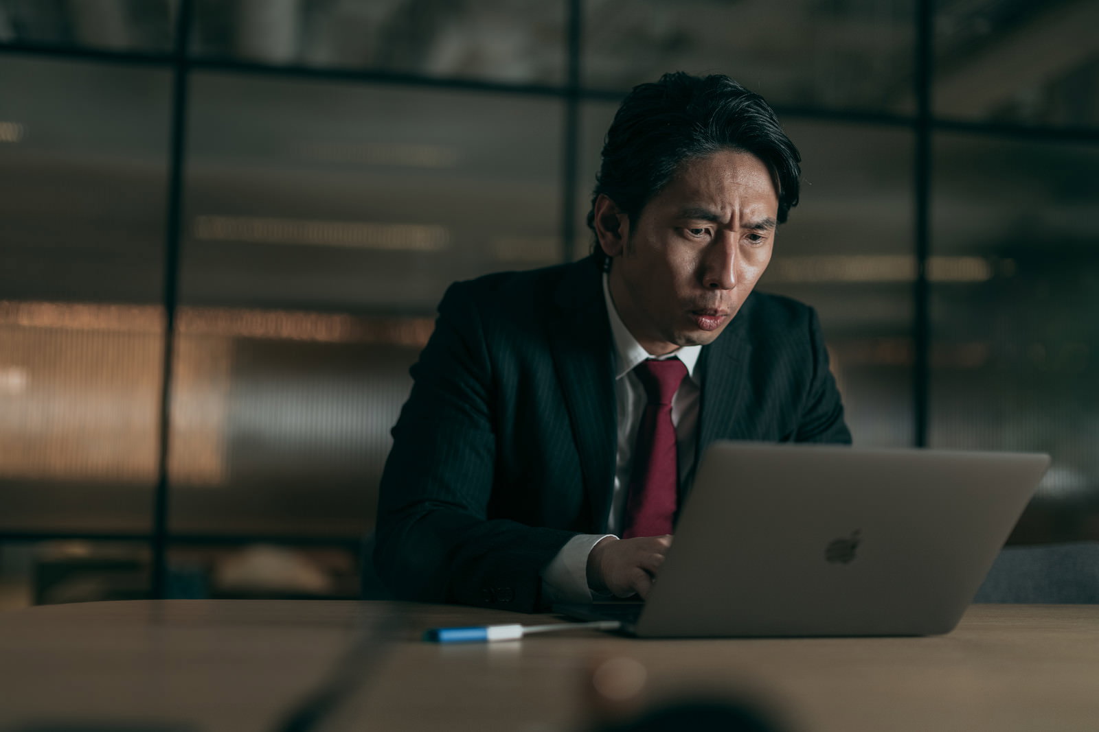 深夜のオフィスでパソコンに向かう疲れた表情のスーツ姿の男性［モデル：大川竜弥］
