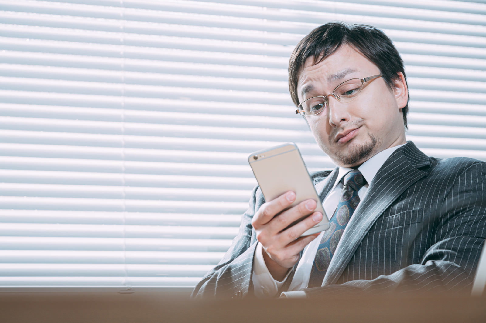 スマートフォンを見て困った表情をするストライプシャツの男性［モデル：Max_Ezaki］