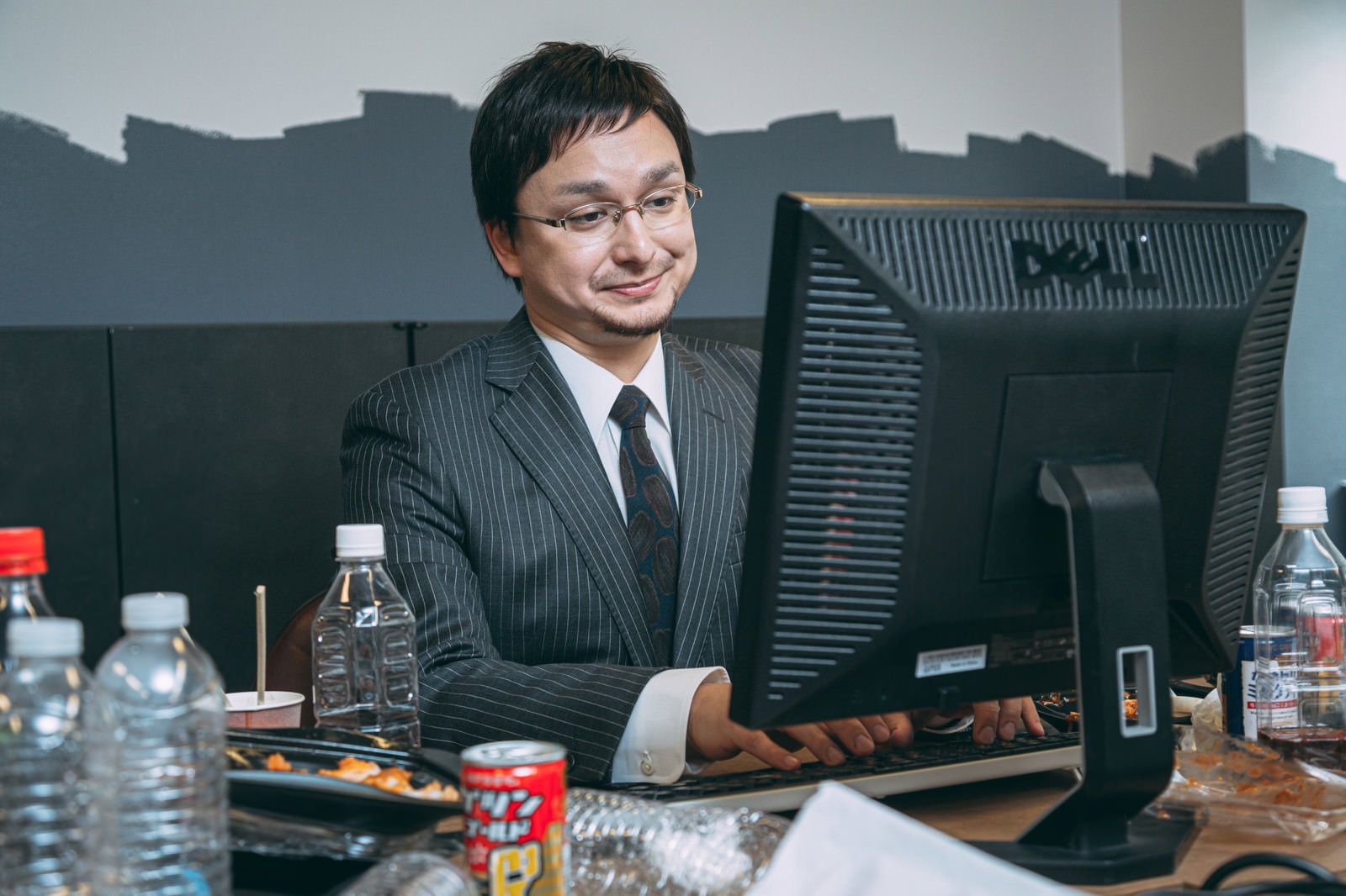 デスクでパソコンを見ながら食事をするスーツ姿の男性［モデル：Max_Ezaki］