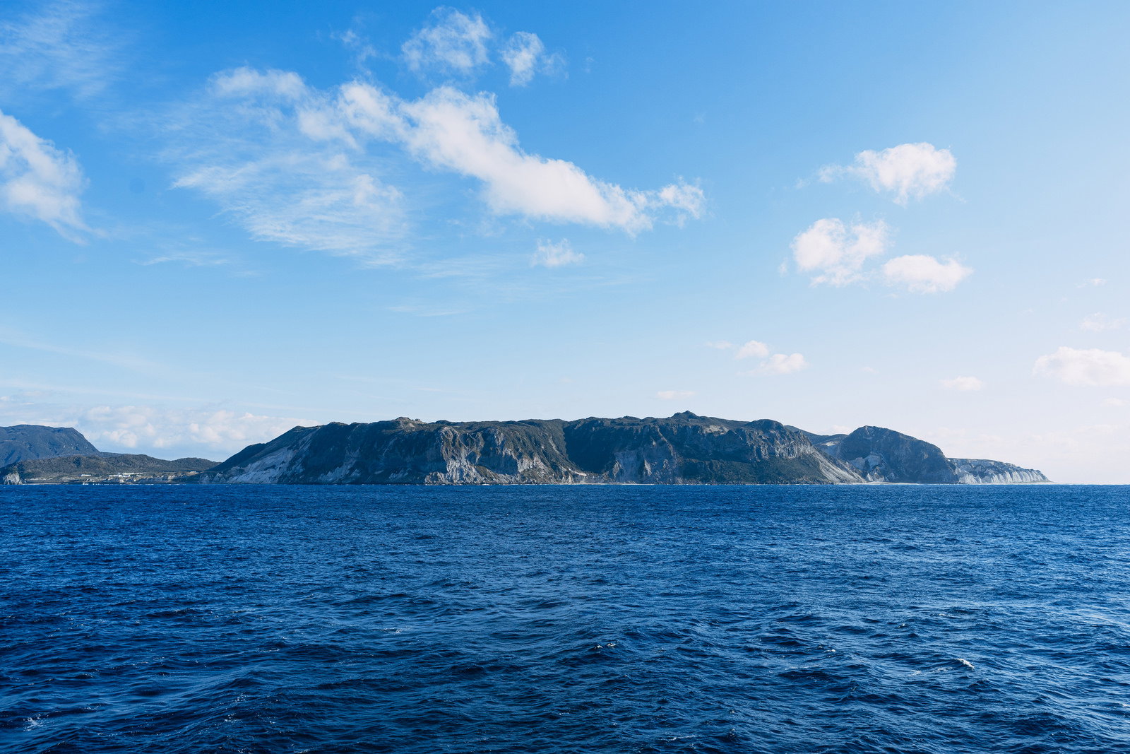 海上から見た伊豆大島の海岸線と緑の斜面、青い海と空の景観写真