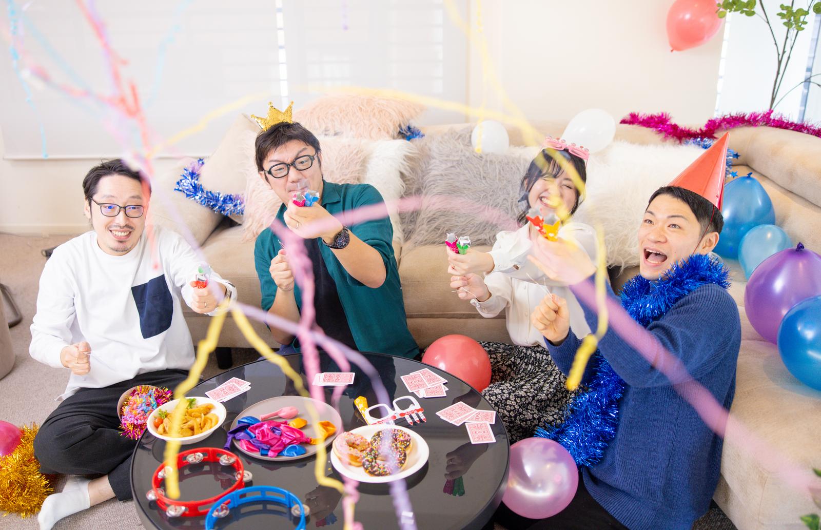 パーティールームで複数の人がクラッカーを鳴らして誕生日パーティーを楽しんでいる［モデル：OZPA ゆうせい 河村友歌 モデルリリース］